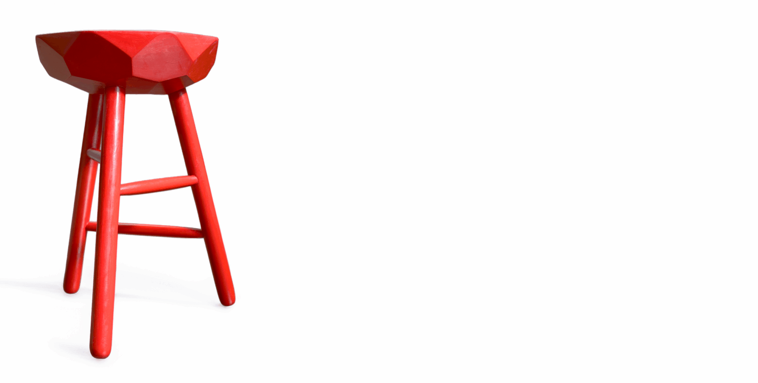 Bright red three-legged wooden stool with geometric diamond-shaped solid wood seat on a white background